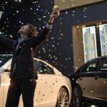 Pessoa feliz comemorando com gráficos e um carro de luxo ao fundo representando a Mega Sena