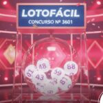 Ilustração 3D de um sorteio da Lotofácil, concurso número 3601. Um globo transparente com bolas numeradas está em destaque contra um fundo rosa vibrante e iluminado, com confetes espalhados.