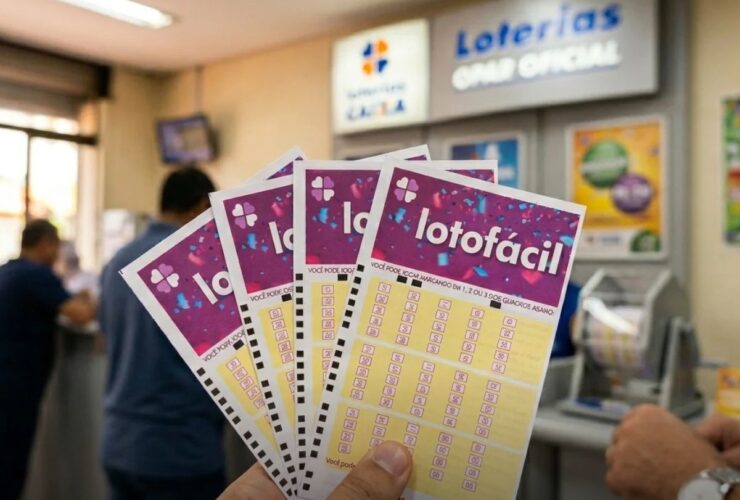 Mão segurando vários volantes da Lotofácil dentro de uma unidade das Loterias Caixa.