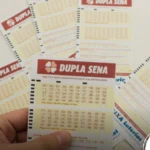 Homem segurando bilhetes da dupla sena com outros soltos em cima da mesa