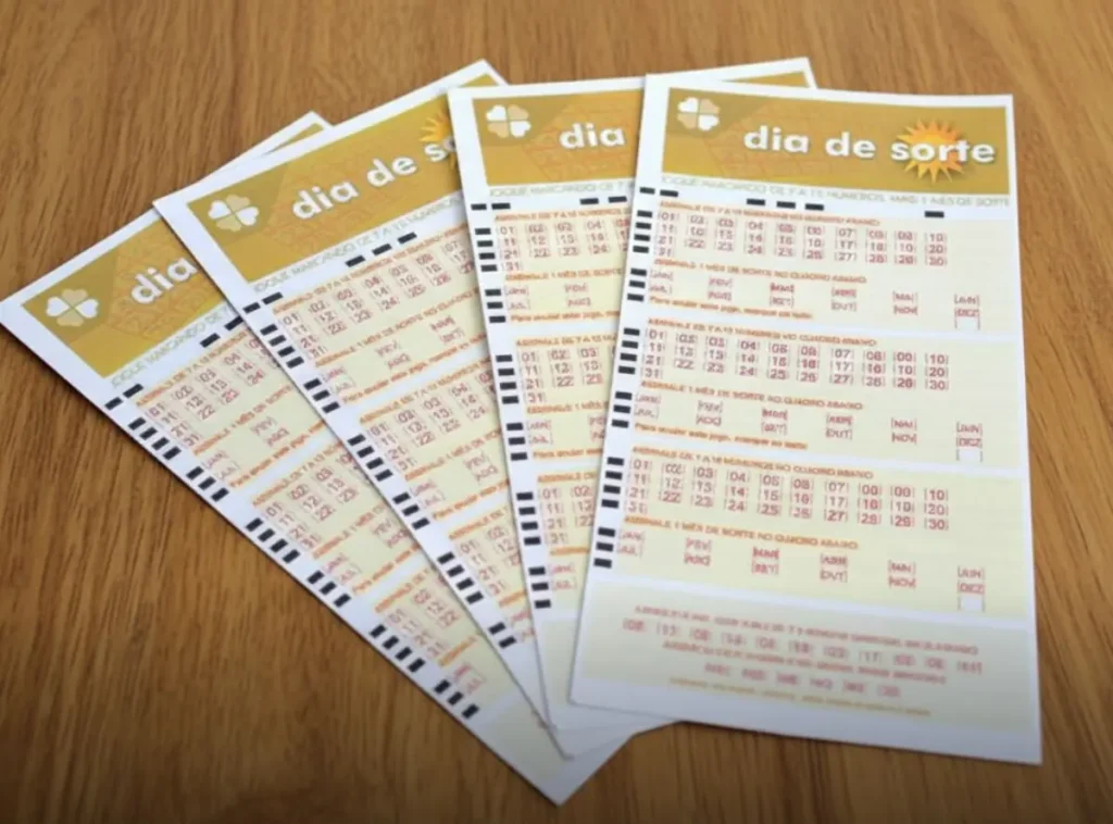Palpites do Dia de Sorte 1277: Confira jogos simulados para o prêmio de R$ 300 mil 11 Quatro volantes da loteria Dia de Sorte organizados em leque sobre uma mesa de madeira clara com iluminação focada.