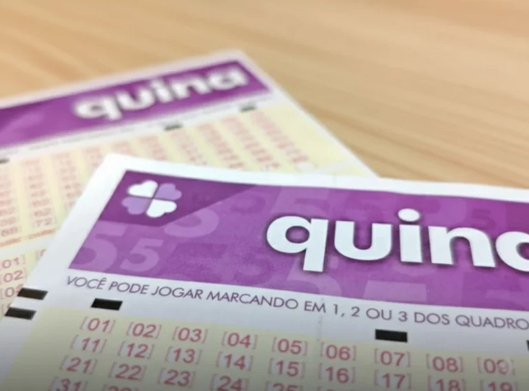 Close-up de dois volantes de apostas de loteria da quina na cor roxa sobre uma mesa de madeira clara com foco seletivo.