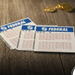 Bilhetes da Loteria Federal sobre superfície de madeira com moedas.