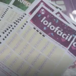 Vários volantes de apostas da Lotofácil da Caixa espalhados sobre uma mesa, mostrando os campos de números de 01 a 25.