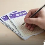 Mão segurando uma caneta preta prestes a marcar um volante de loteria da Quina