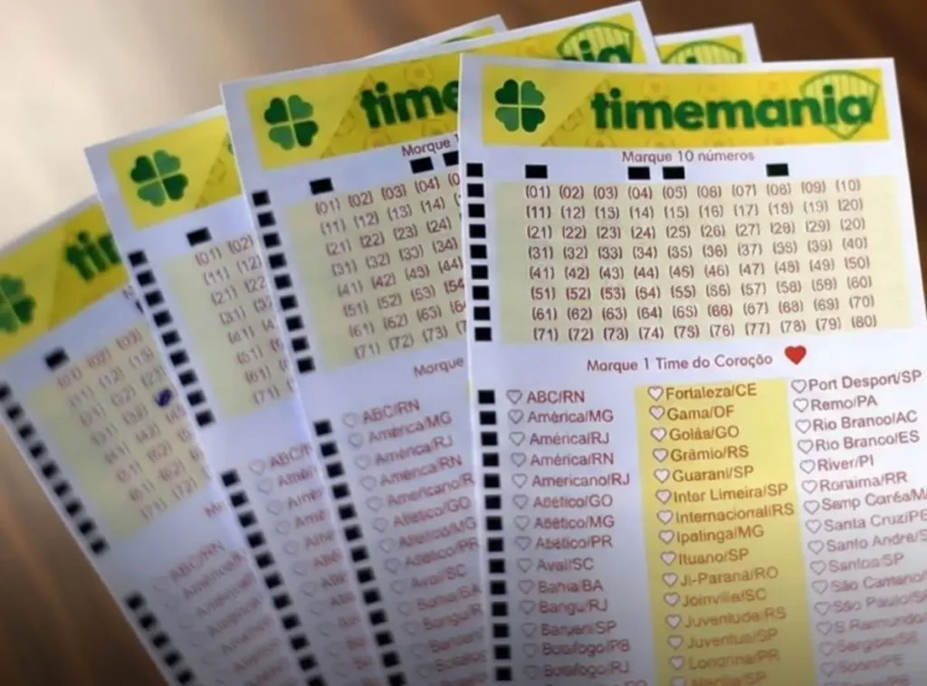 Timemania 2430 acumula: Ninguém cravou as 7 dezenas e prêmio sobe para R$ 9,30 milhões 12 Quatro volantes de apostas da Timemania em leque sobre uma mesa de madeira escura com iluminação clara e nítida.