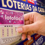 Foto de uma mão pegando um bilhete da Lotofácil em lotérica
