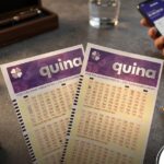 Volantes da Quina em destaque com um smartphone ao fundo mostrando um aplicativo de apostas e uma caneta.