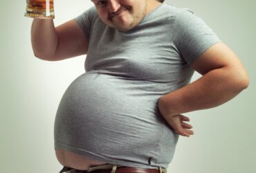 Pessoa com barriga grande segurando copo de cerveja - Fotos do Canva