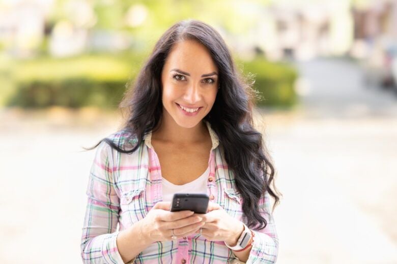 A smiling brunette is writing messages on her mobile phone. A young woman reads received messages and writes back on a smartphone. - Fotos do Canva