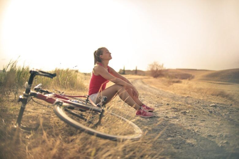 Mulher esportiva com bicicleta descansando em uma estrada rural sob a luz do sol - Fotos do Canva