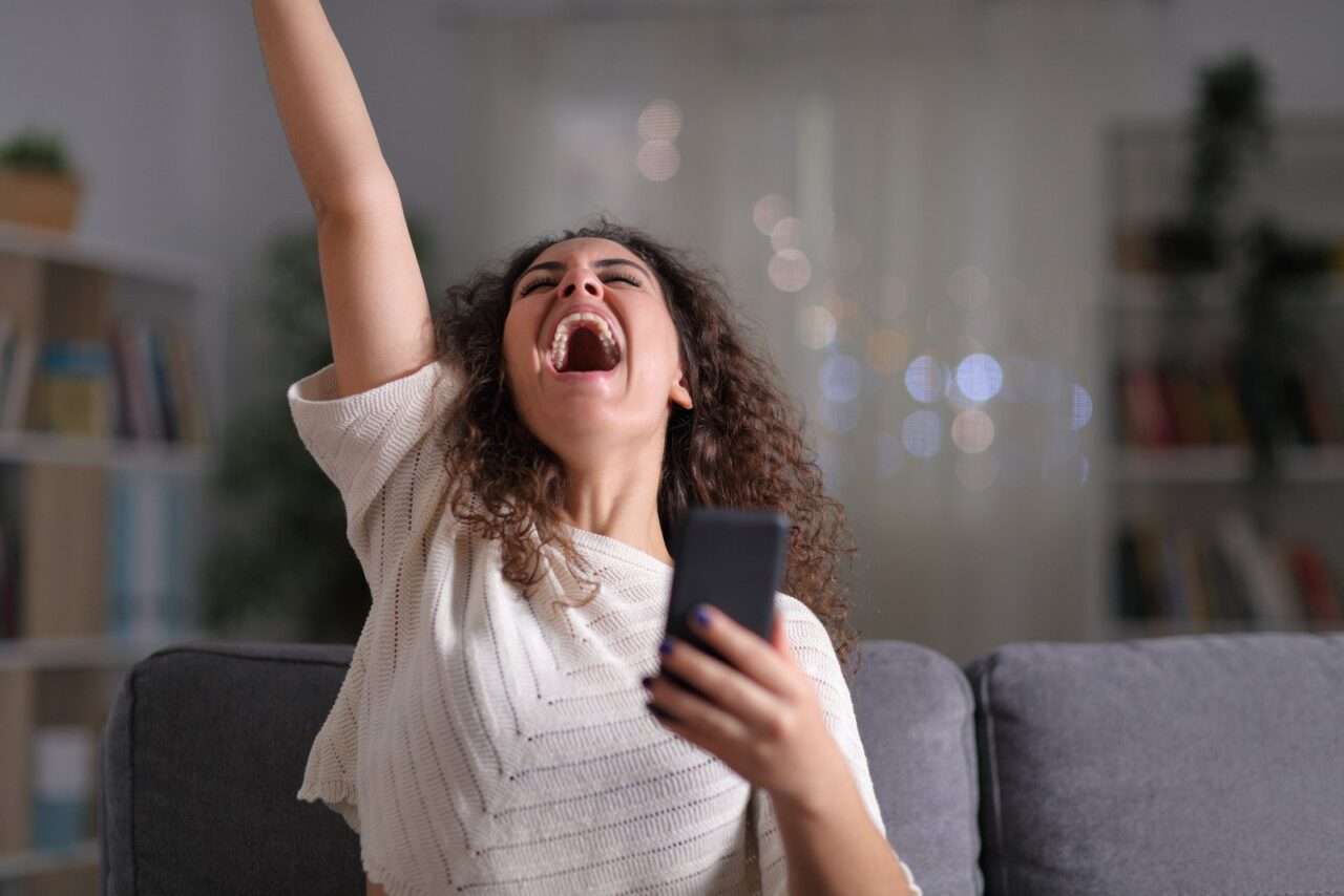 Animado mulher comemorando sucesso segurando o telefone móvel - Fotos do Canva