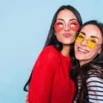 Amigos para sempre. Duas amigas lindas e adoráveis em óculos de sol posando com sorriso no fundo azul - Fotos do Canva