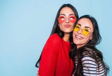 Amigos para sempre. Duas amigas lindas e adoráveis em óculos de sol posando com sorriso no fundo azul - Fotos do Canva