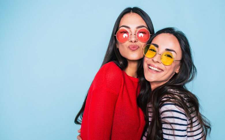 Amigos para sempre. Duas amigas lindas e adoráveis em óculos de sol posando com sorriso no fundo azul - Fotos do Canva