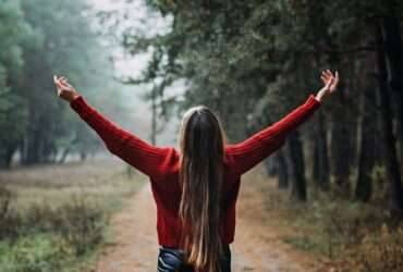 Uma jovem sozinha com cabelos longos e esvoaçantes expressa emoções na floresta - Fotos do Canva