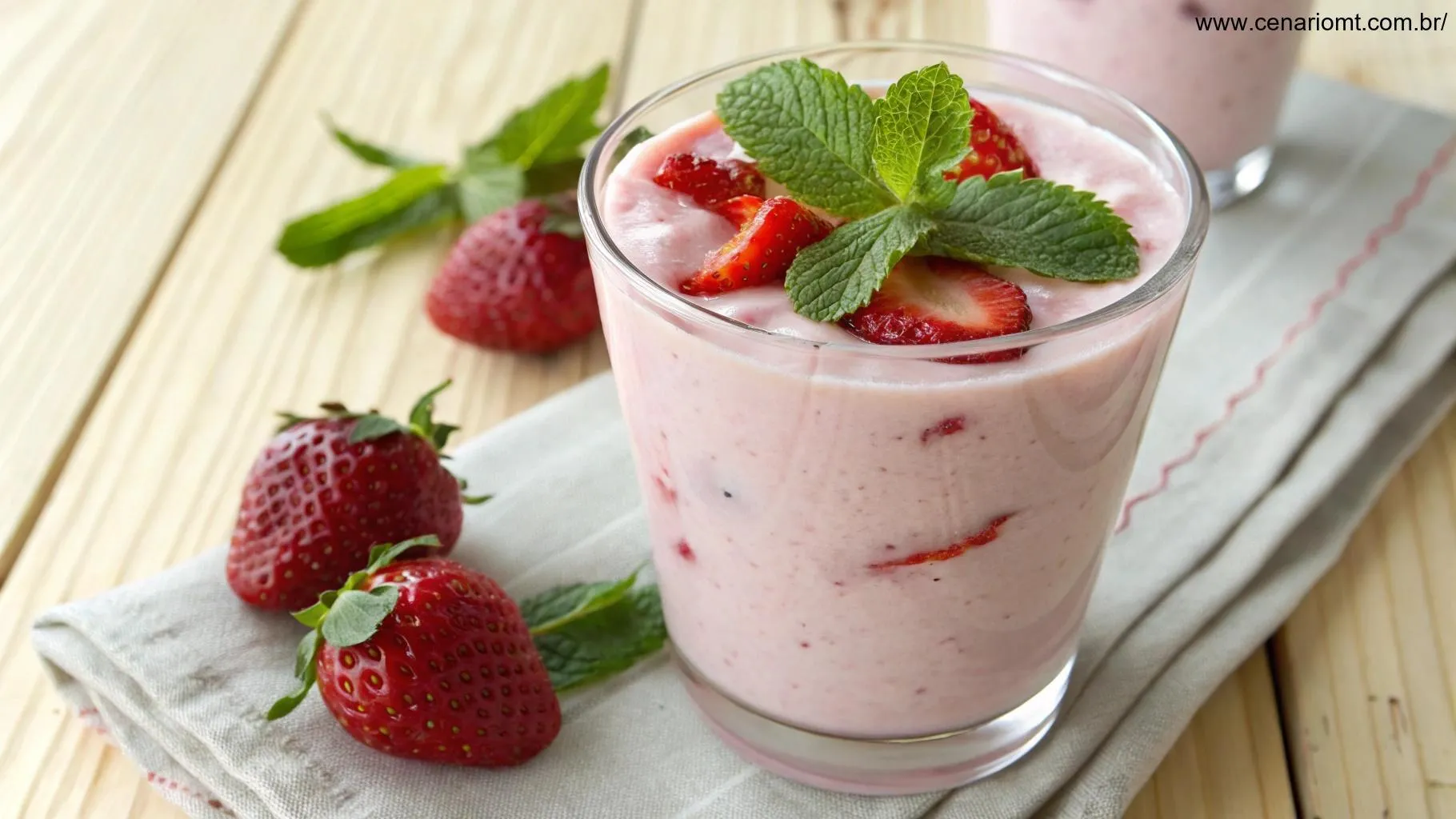 Smoothie cremoso de morango com iogurte servido em um copo transparente com morango e folha de hortelã