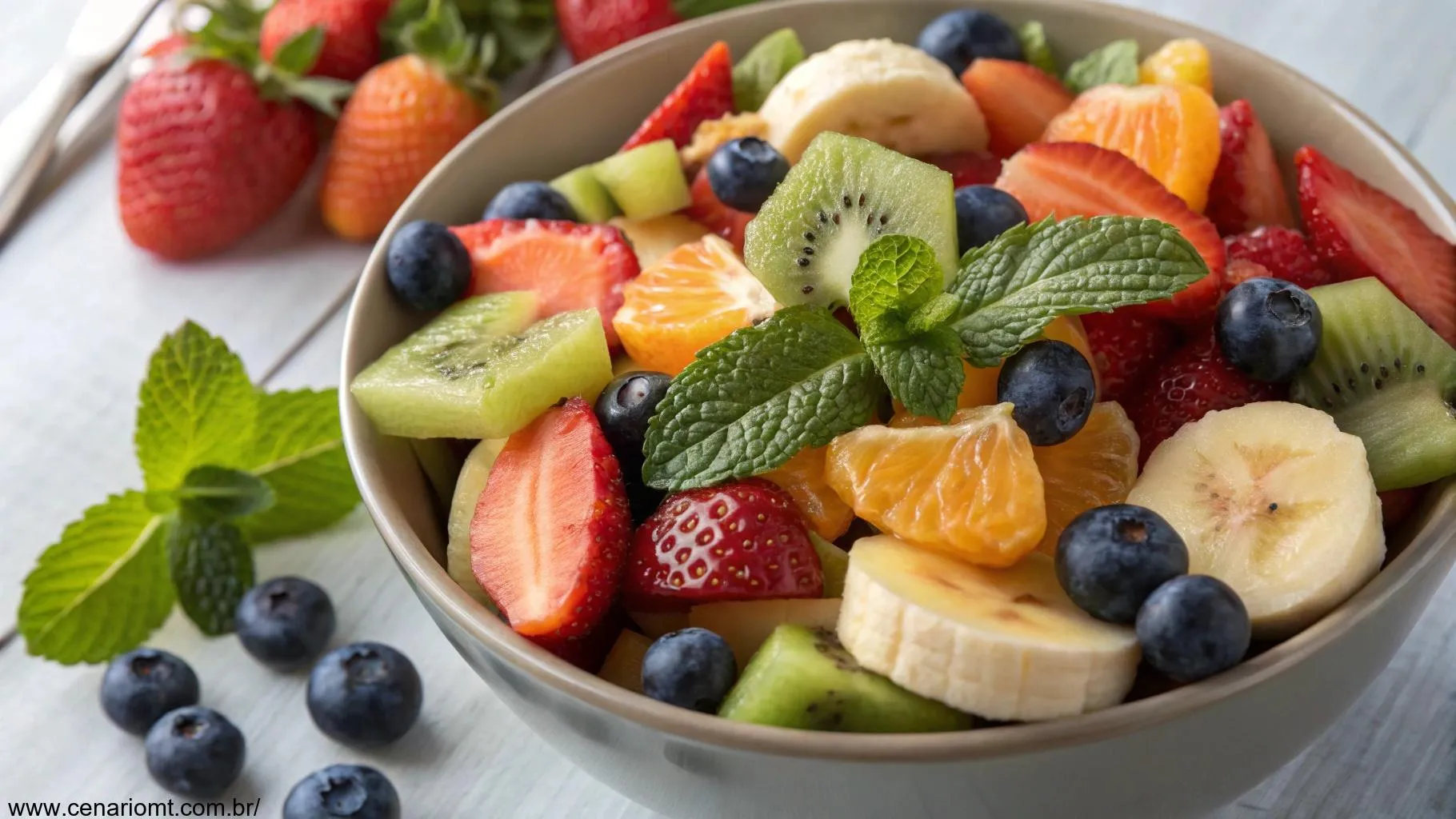 Uma salada de frutas frescas com frutas coloridas como morangos, mirtilos, laranjas, bananas e kiwis, dispostas de forma organizada em uma tigela, com folhas de hortelã como enfeite.