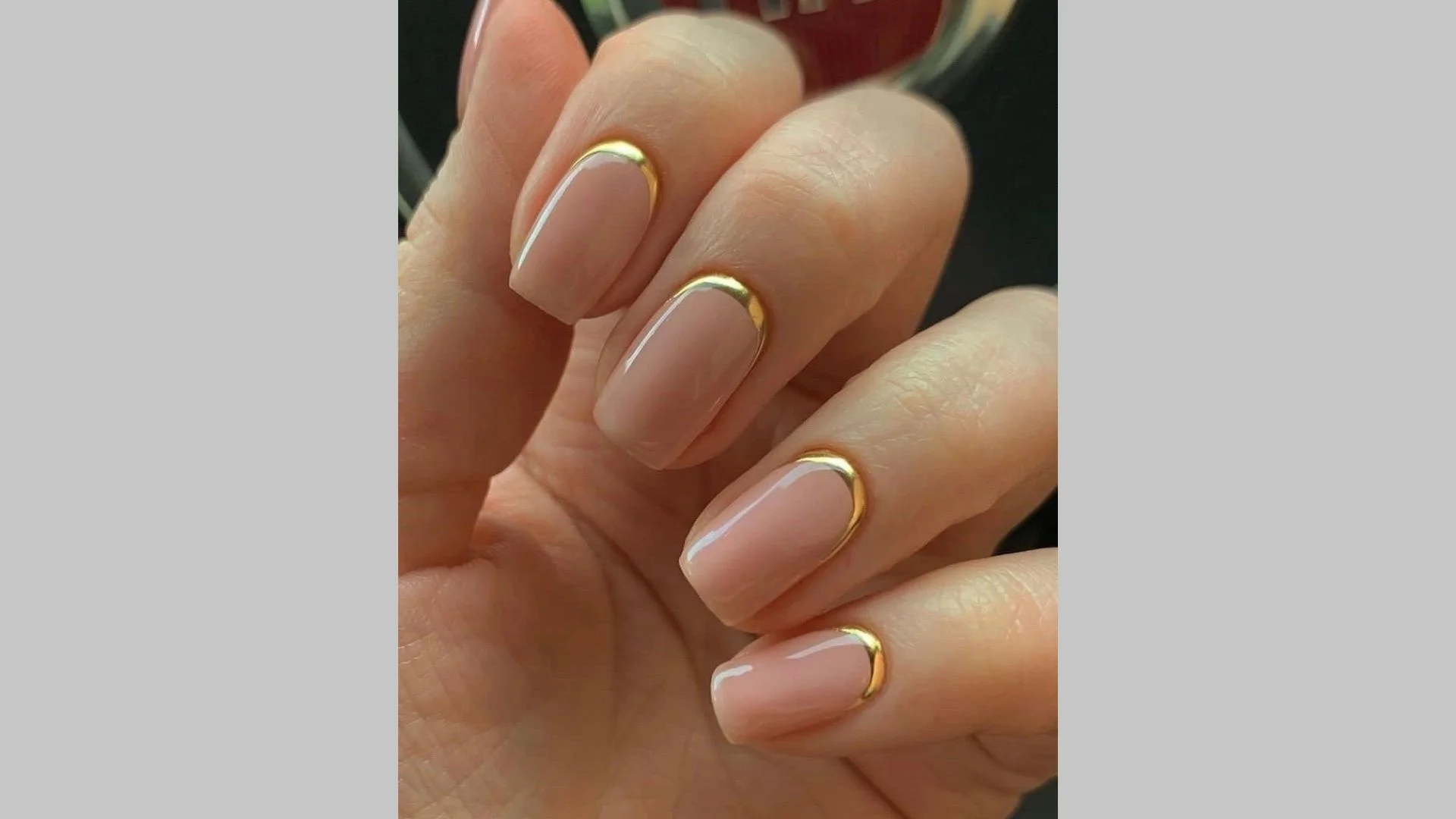 Manicure minimalista com detalhes dourados em unhas nude.