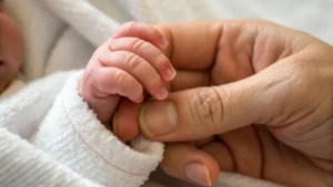 Uma foto de um bebê recém nascido segurando o dedo da mãe