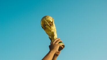Troféu da Copa do Mundo da FIFA sendo erguido por mãos contra o céu azul
