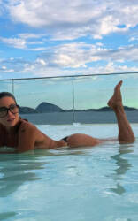 Danielle Winits posa de biquíni preto em piscina durante tarde ensolarada.