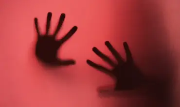 Imagem de mãos de mulher tocando vidro vermelho simbolizando abuso