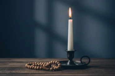 Vela acesa e terço católico representando a oração da noite e a paz espiritual.