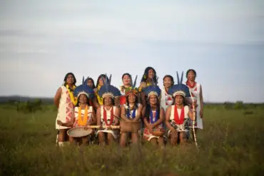 Mulheres indígenas do povo Kurâ-Bakairi reunidas durante a gravação do álbum Kâremu, destacando instrumentos tradicionais e sorrisos, em ambiente de preservação cultural.