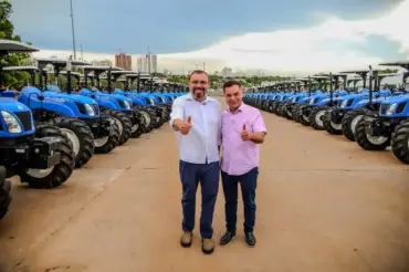 Fileira de tratores novos de cor azul estacionados no pátio da Arena Pantanal em Cuiabá para entrega à agricultura familiar.