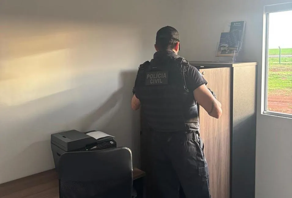 Policial civil de costas, usando colete com a inscrição "Polícia Civil", realiza busca em armário de escritório durante a Operação Agro-Fantasma em Mato Grosso.