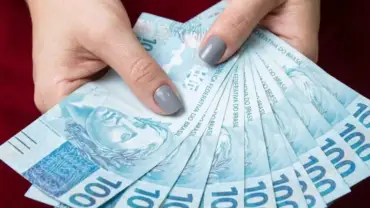 Mulher segurando notas de cem reais na mão.