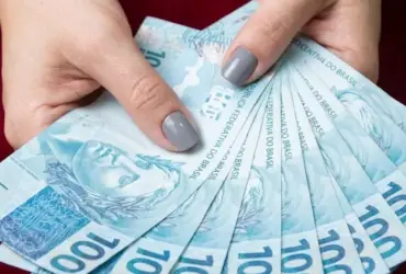 Mulher segurando notas de cem reais na mão.