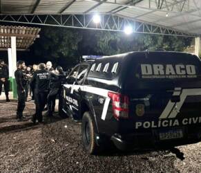 Policiais civis ao lado de viatura da DRACO