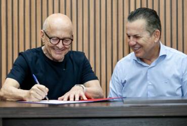 Otaviano Pivetta e Mauro Mendes rindo enquanto assinam documento