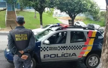 Foto de policial militar ao lado de viatura estacionada