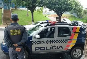 Foto de policial militar ao lado de viatura estacionada