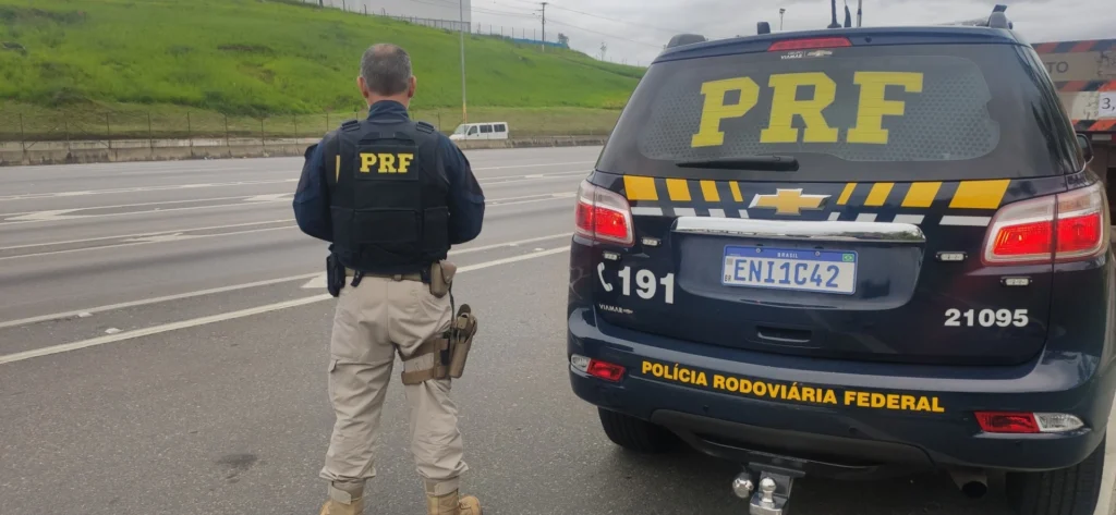 Oficial da PRF ao lado de viatura