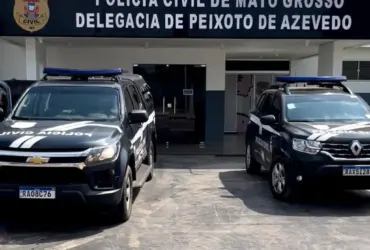 Foto da fachada da delegacia de Polícia Civil de Peixoto de Azevedo, duas viaturas pretas estão estacionadas na frente