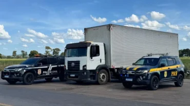 Caminhão apreendido cercado por duas viaturas, uma da polícia civil e outra da PRF