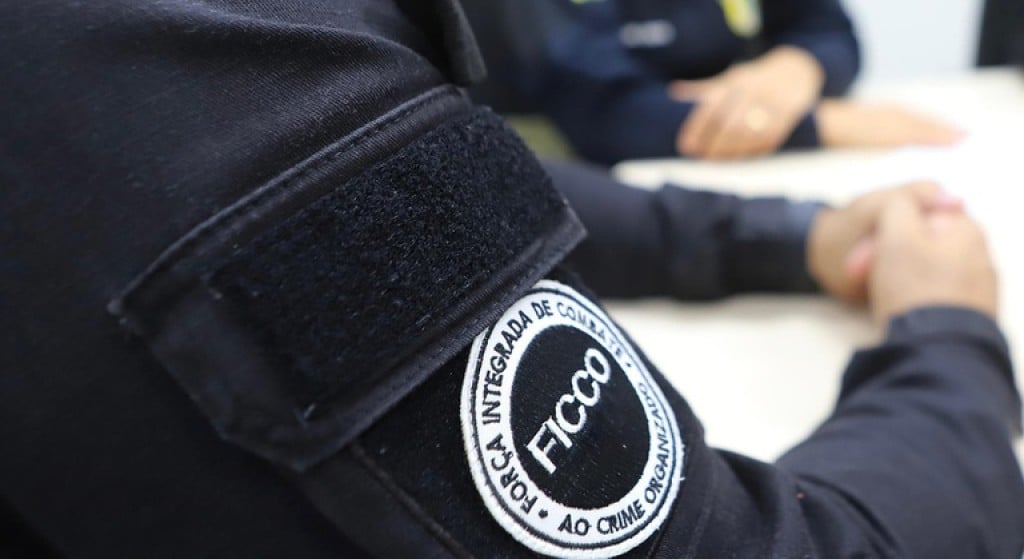 Policial da Ficco sentado em uma mesa, a foto foca no brasão do braço do agente