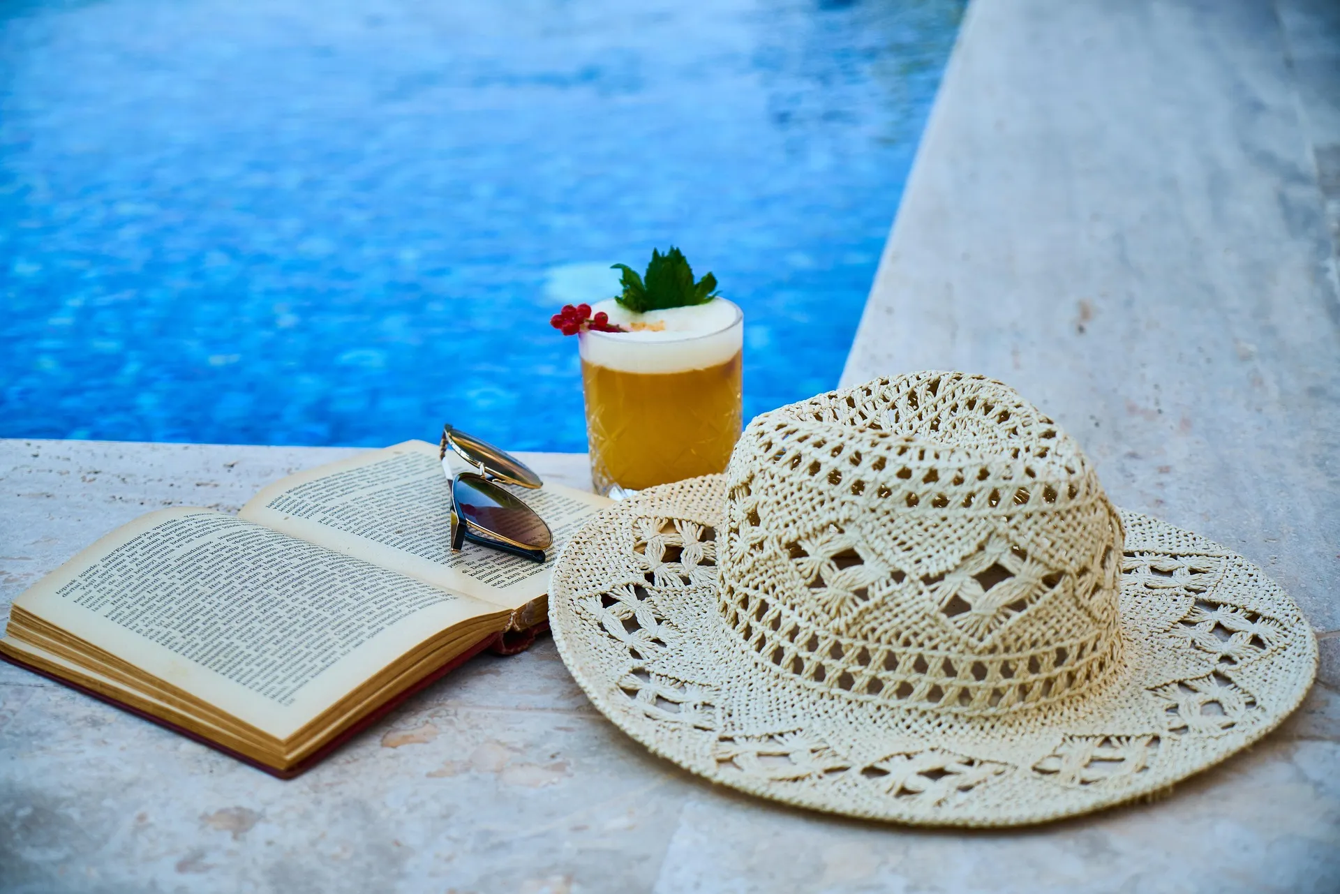Imagem de chapeu e livro à beira da piscina